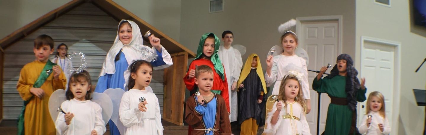 Kids in christmas play outfits on stage smiling and ringing bells