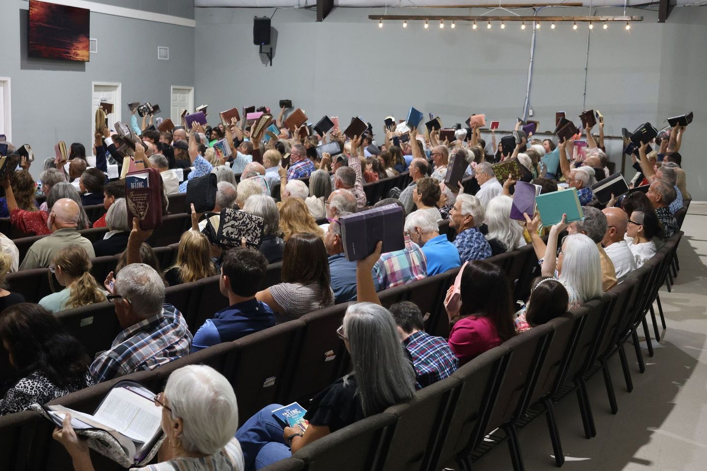 A Large congregation holding up their bibles, viewed from back of room