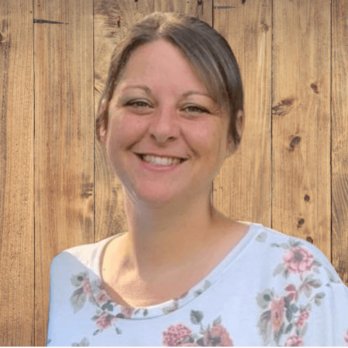 Woman smiling, wearing floral top, wooden background.