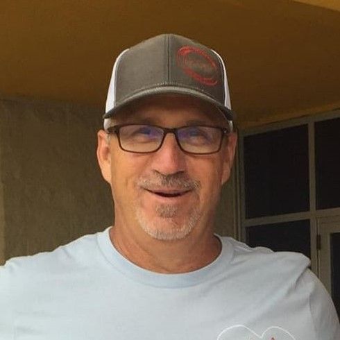 Man wearing glasses and a gray hat smiles outdoors.