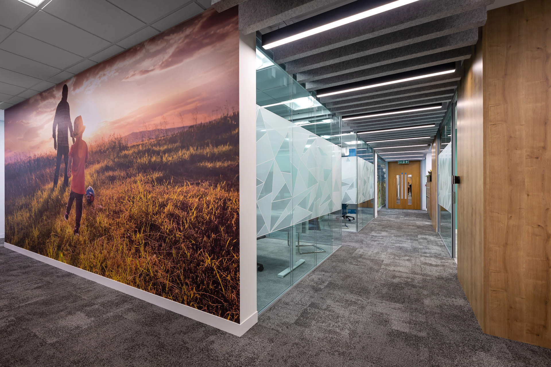 A hallway with a large picture on the wall of a couple walking in a field.