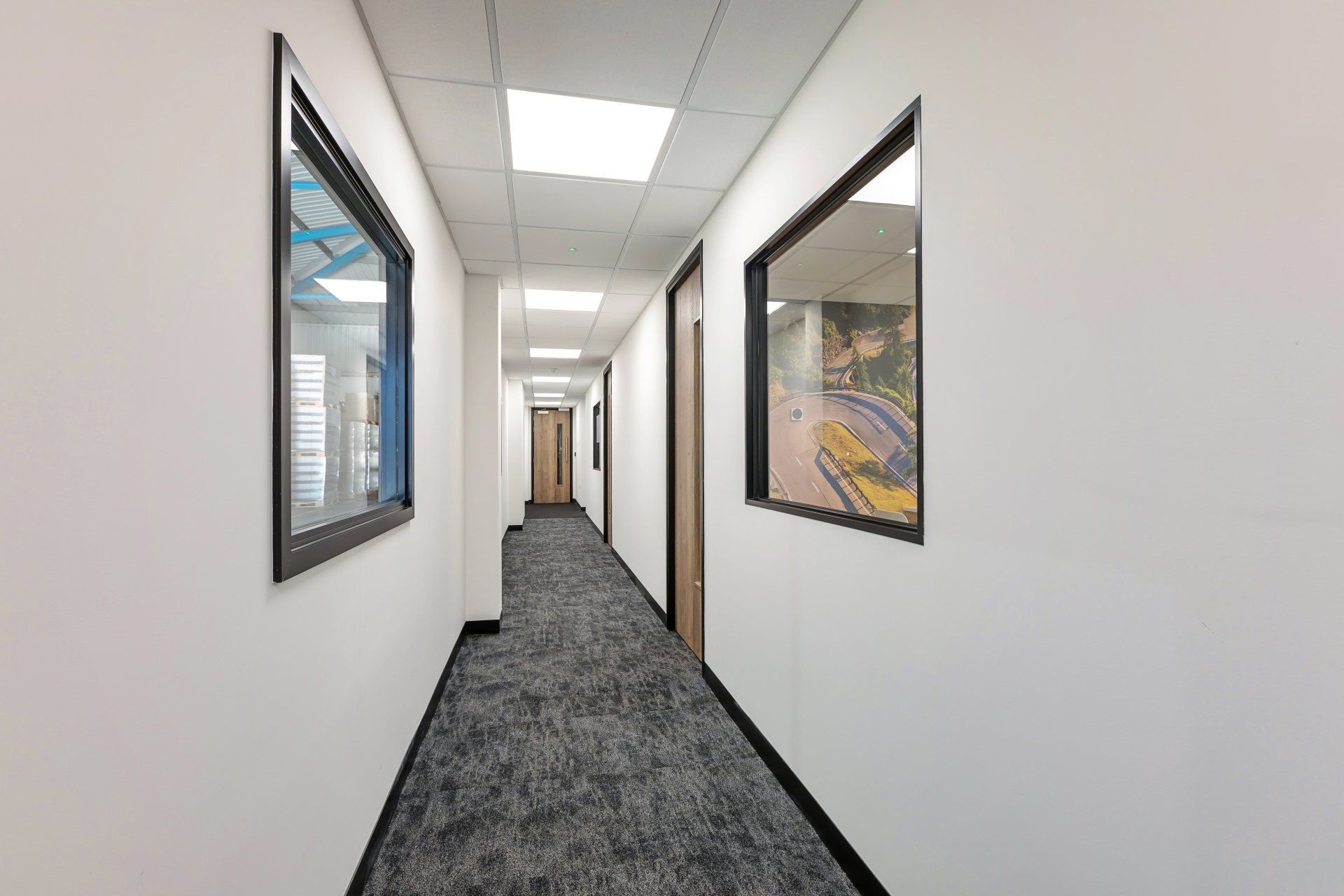 A long hallway with a carpeted floor and two windows on the wall.
