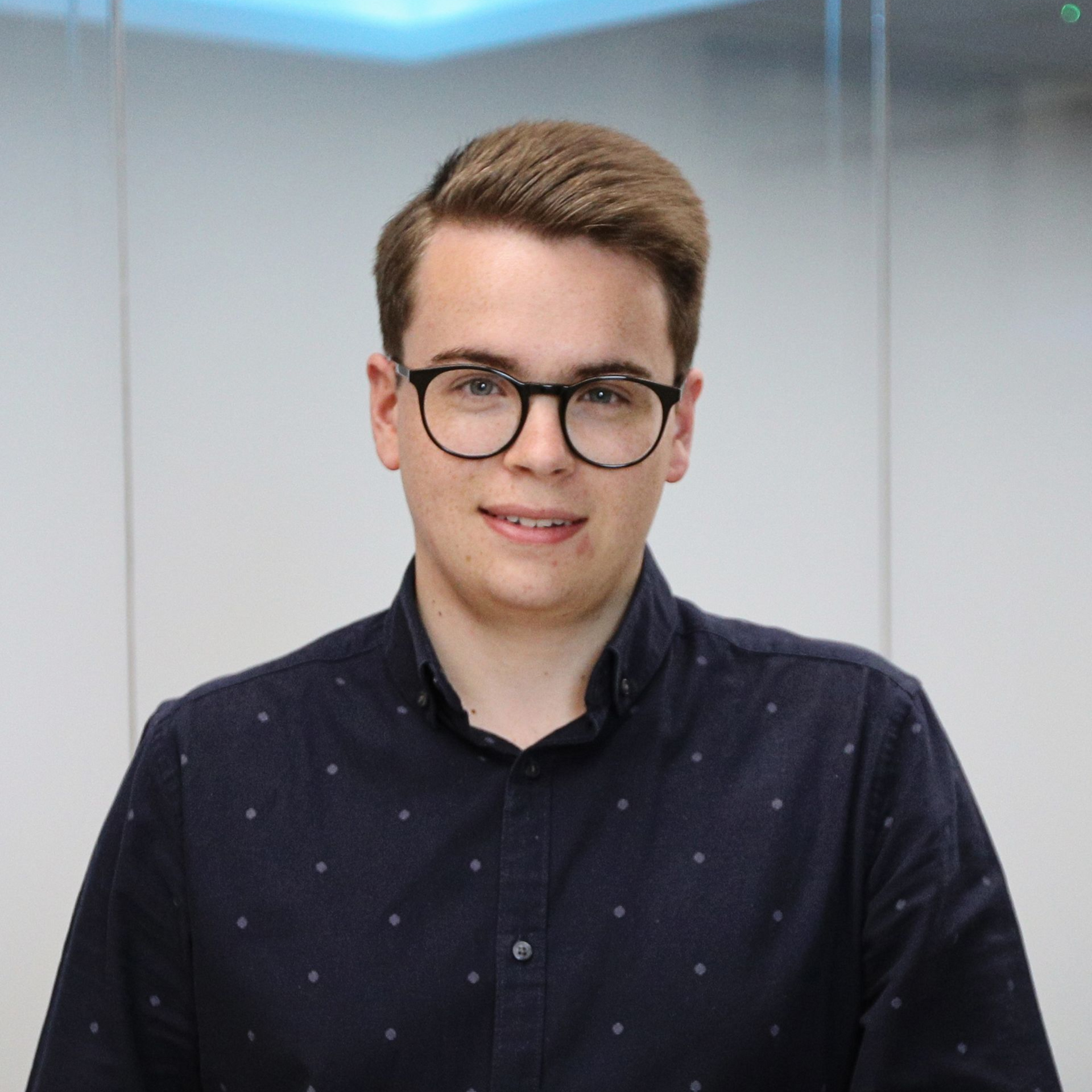 A man in a navy blue shirt is standing in front of a glass wall.