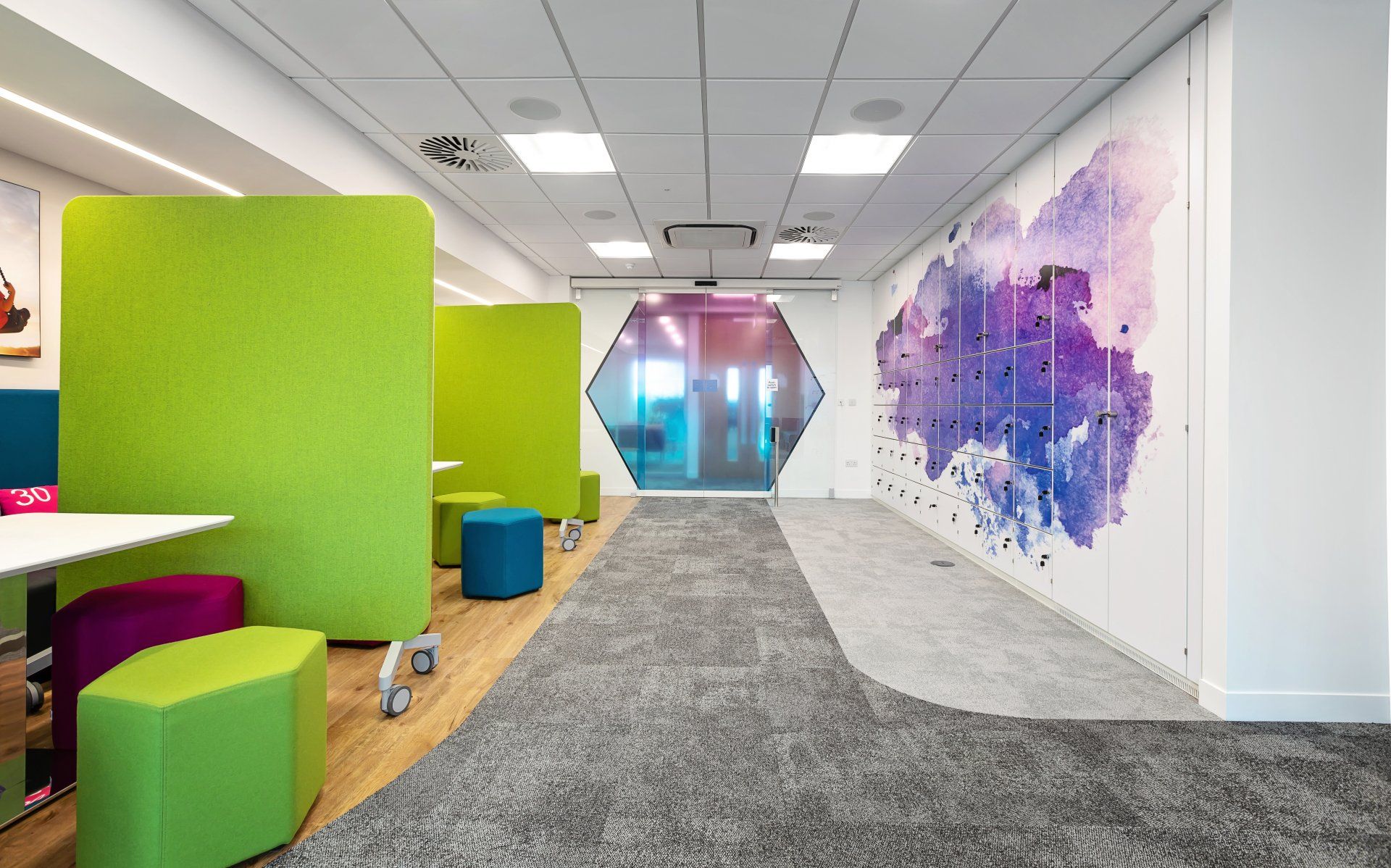 A hallway with green dividers and purple ottomans and a painting on the wall.