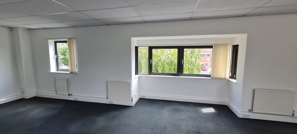 An empty room with two windows and a black carpet.