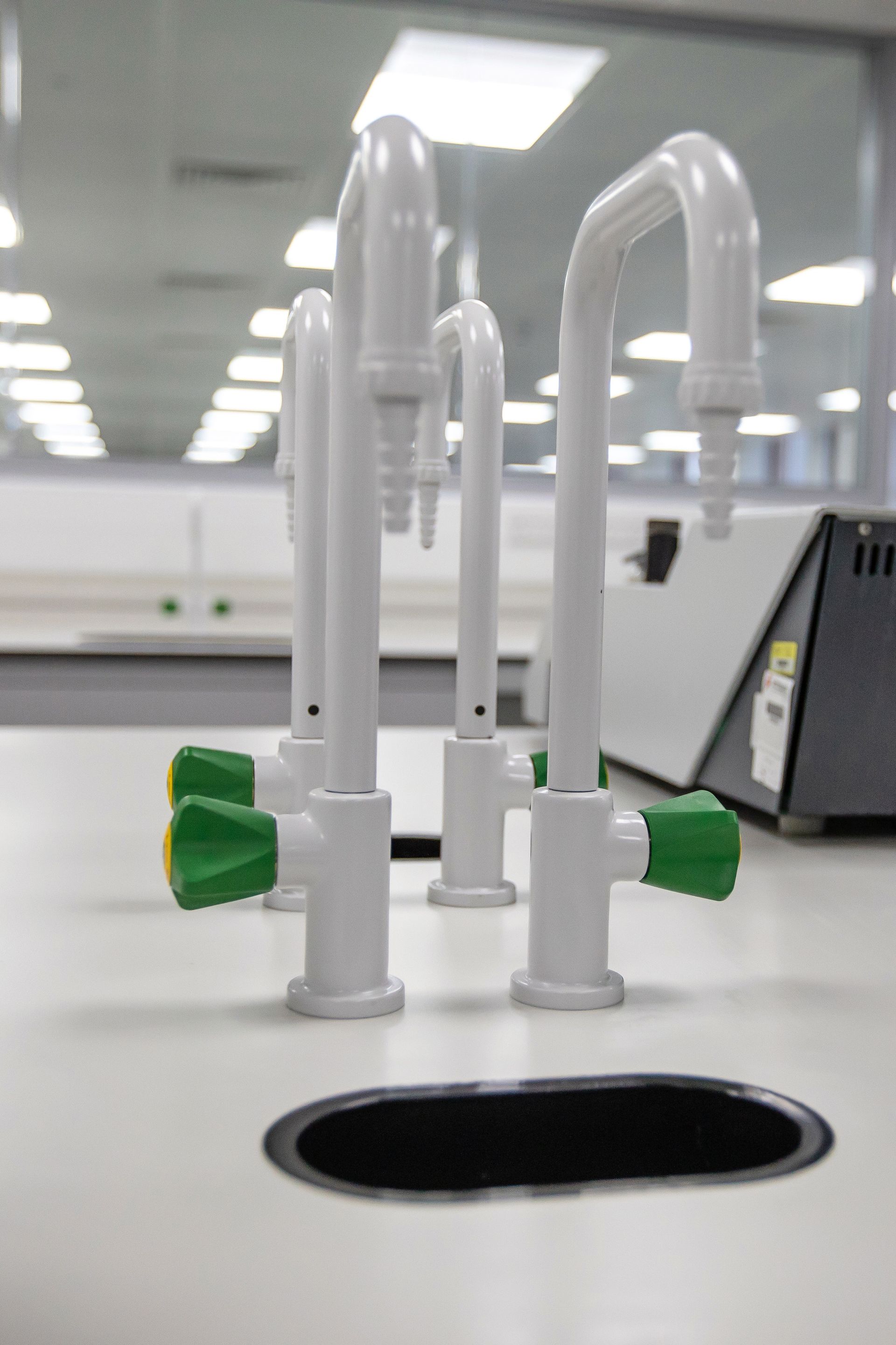 A row of white faucets with green handles are sitting on top of a white counter.