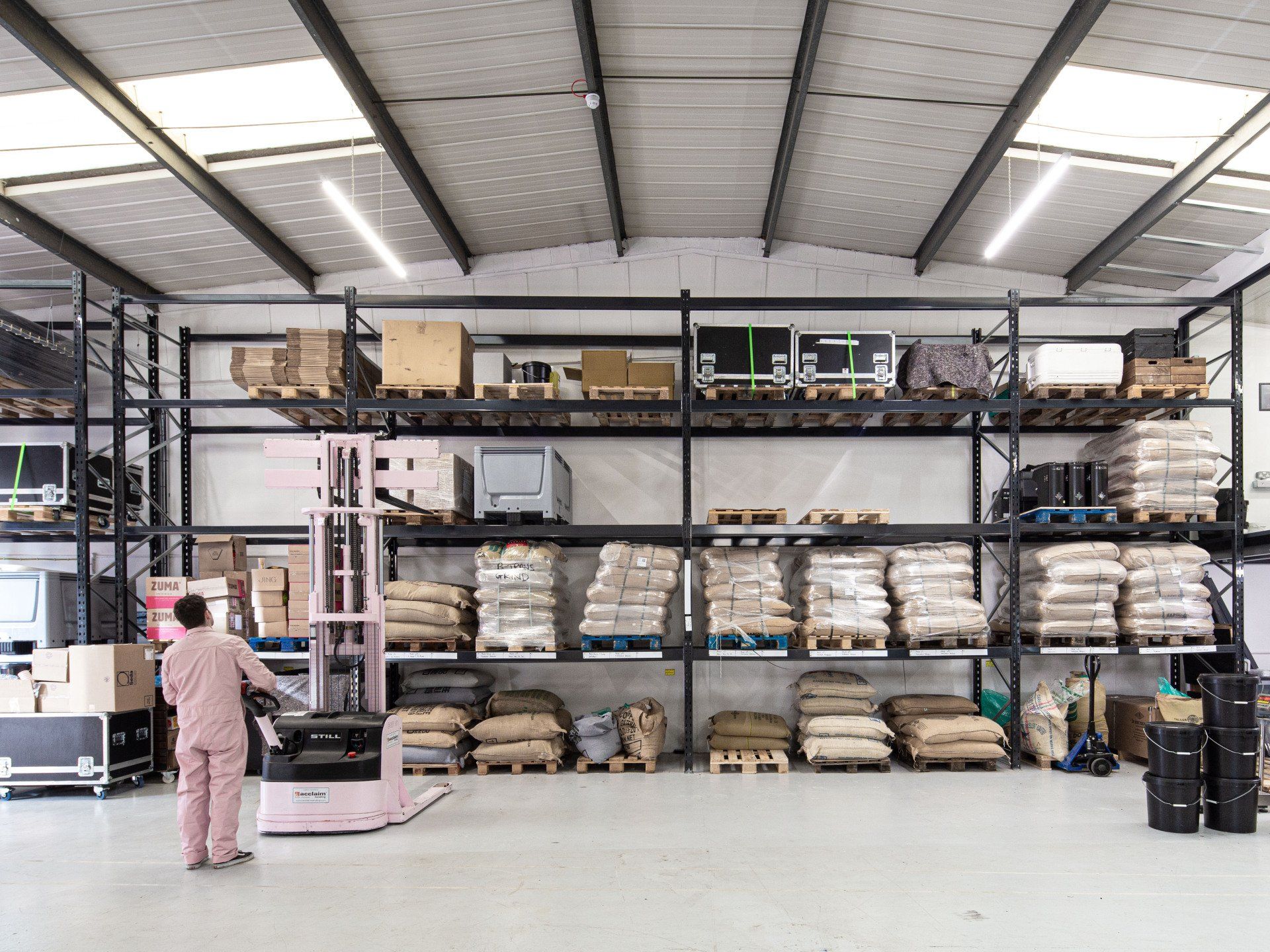 A man is standing in a large warehouse with a forklift.