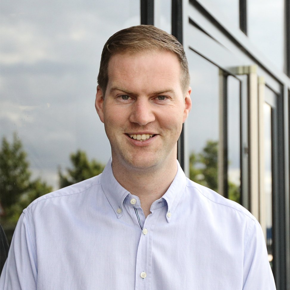 A man in a blue shirt is smiling in front of a building