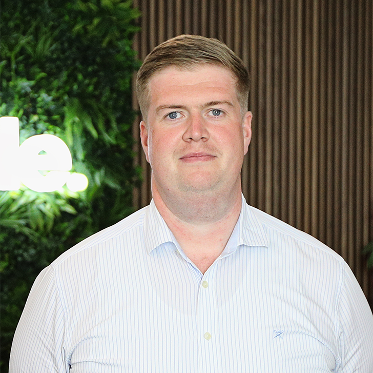 A man in a white shirt is standing in front of a green wall.