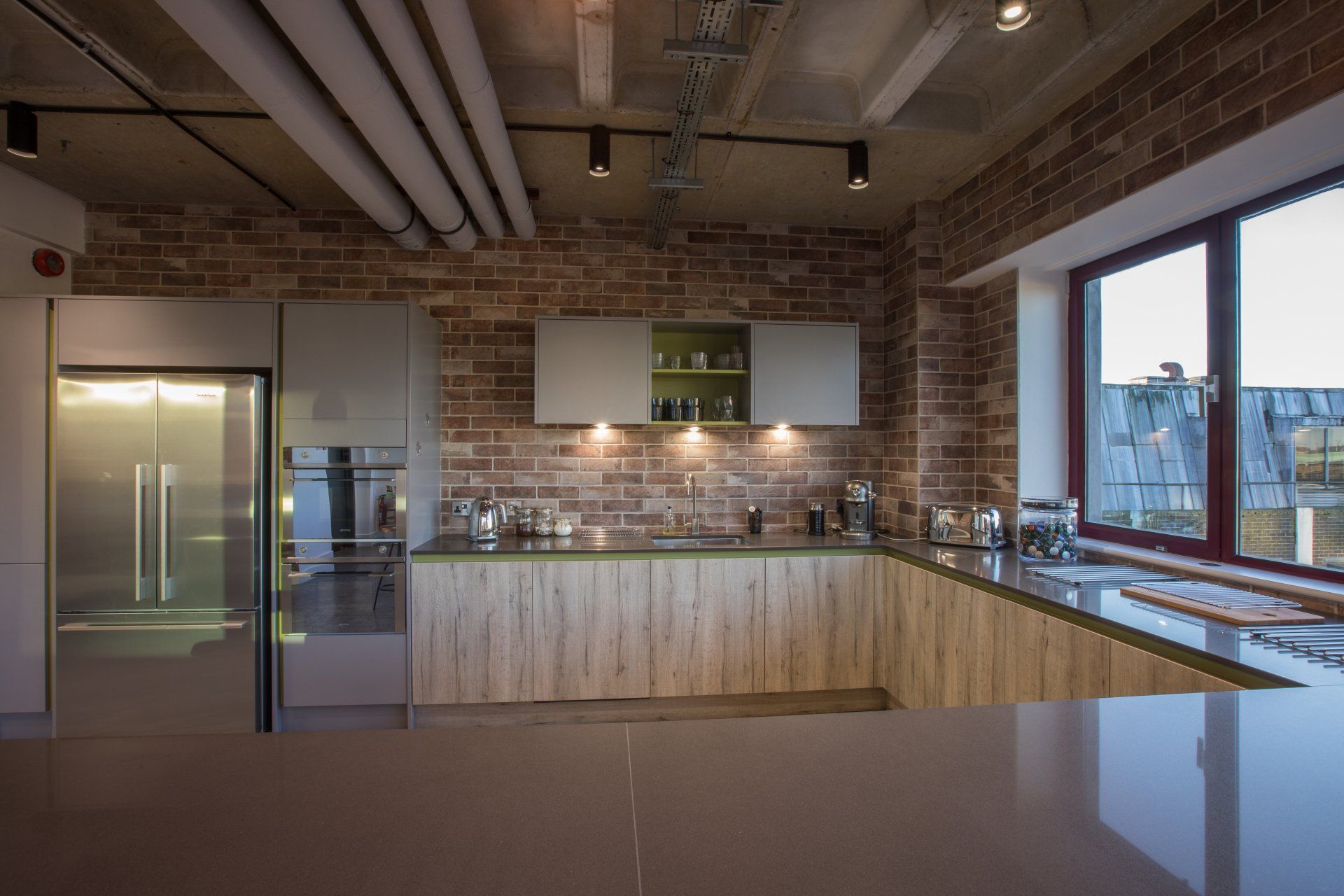 A kitchen with a brick wall , wooden cabinets , stainless steel appliances and a large window.