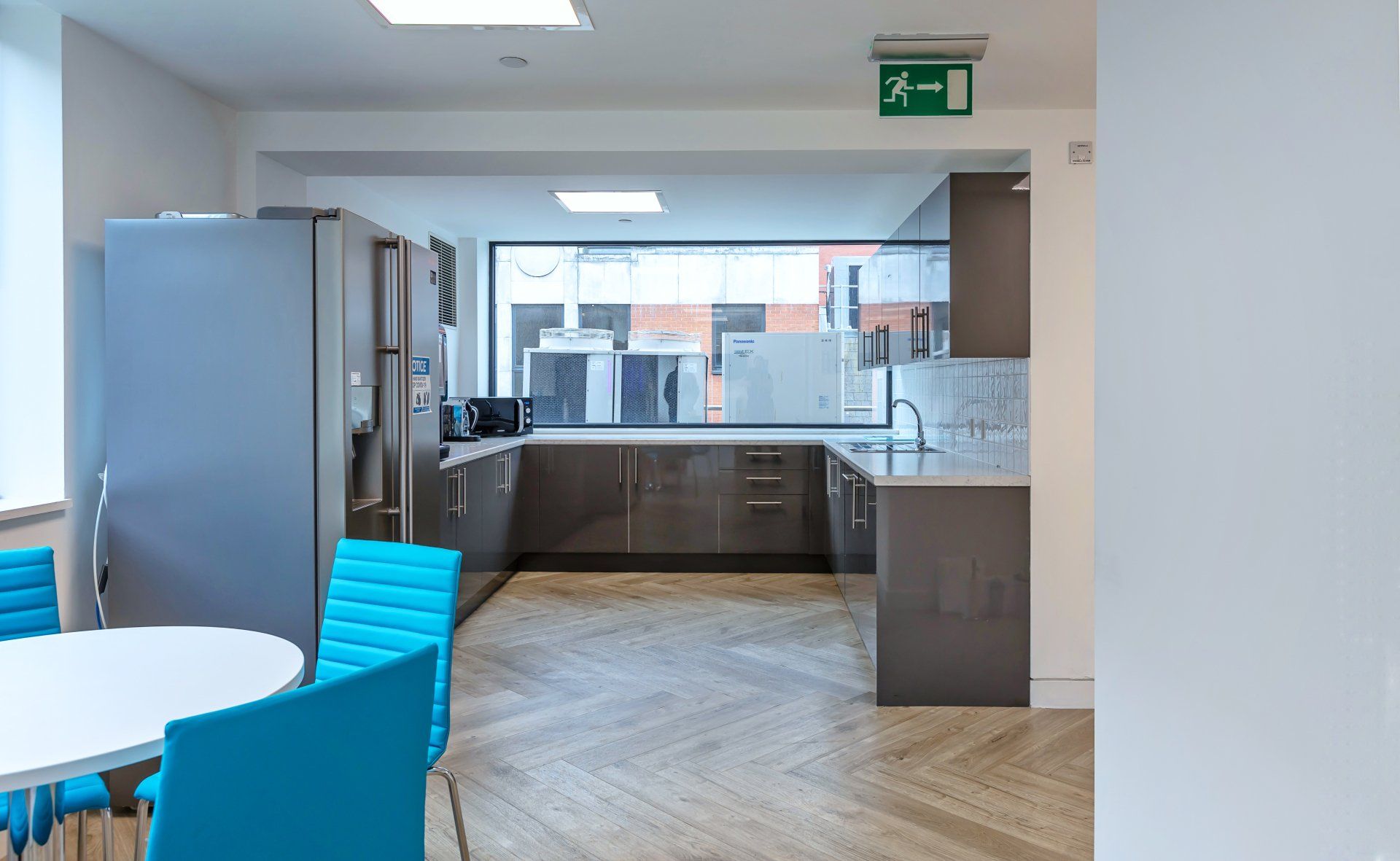 A kitchen with a table and chairs and a green exit sign.