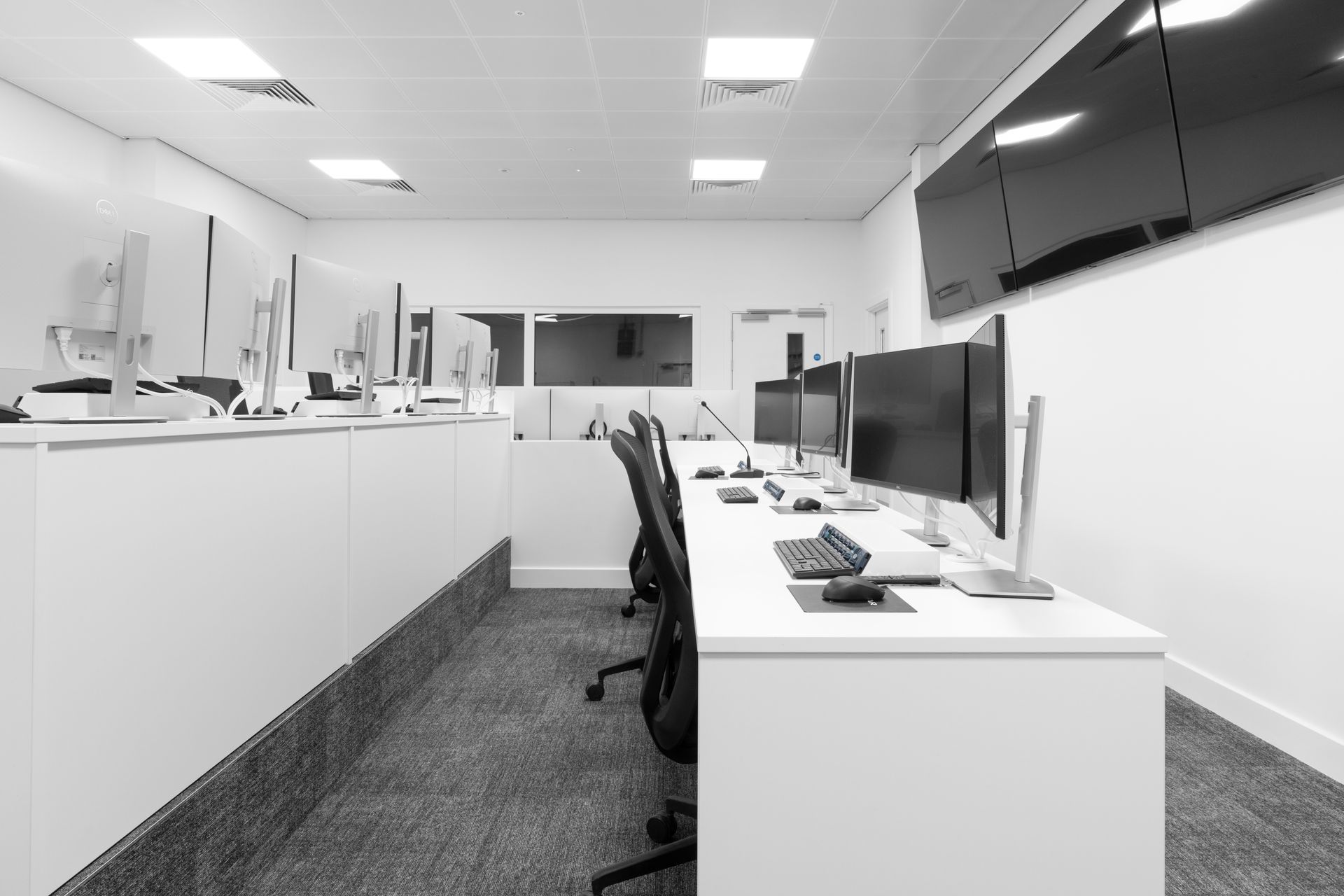 a black and white photo of an office with a lot of computers and chairs .