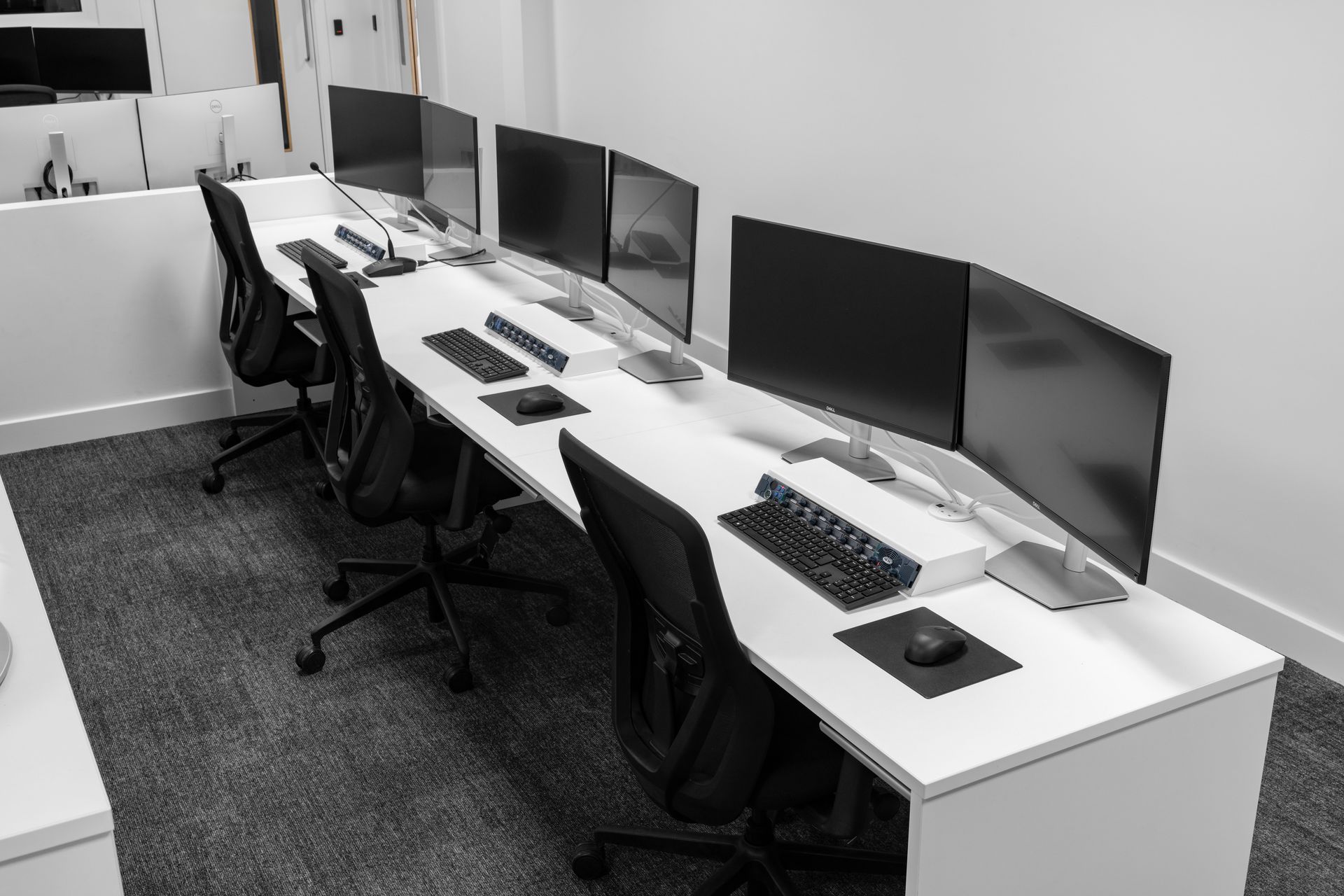 a black and white photo of a row of desks with computers and chairs .