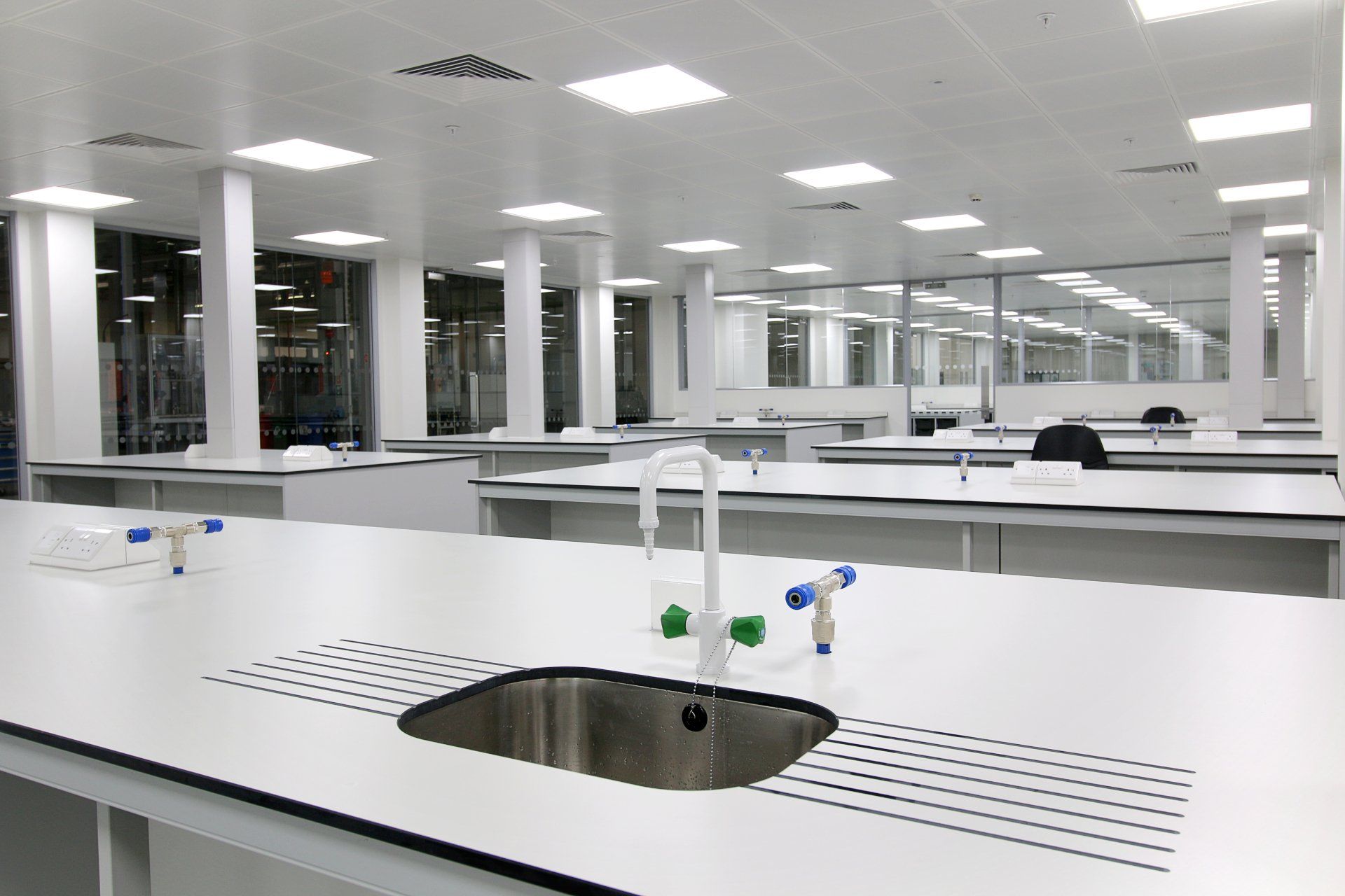 A stainless steel sink is on a white counter in a laboratory.