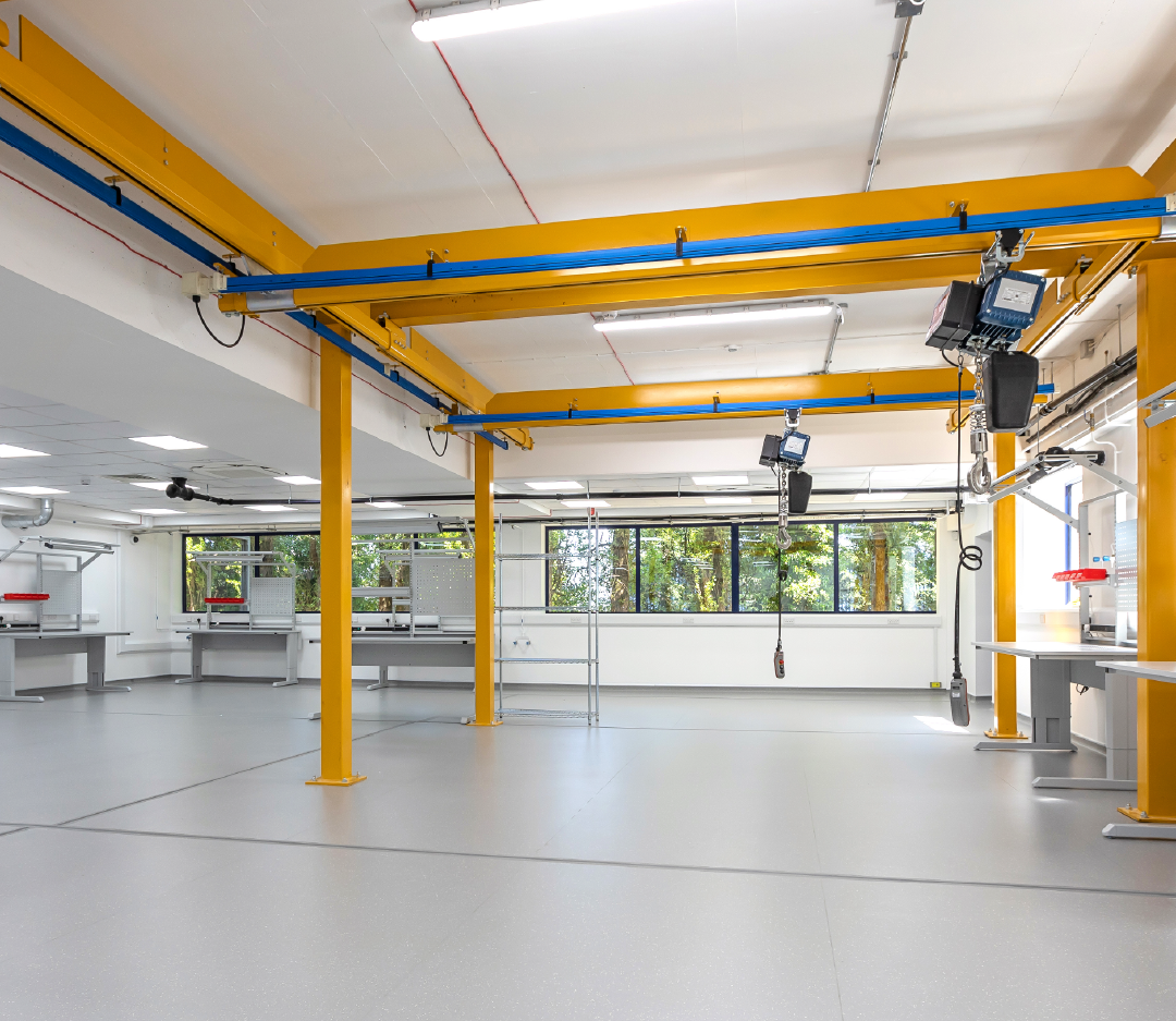 Yellow and grey industrial space with overhead crane system and work tables.