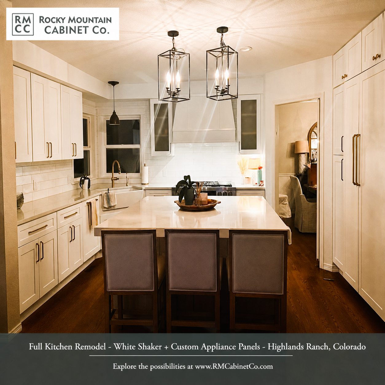 A bright, modern kitchen features white cabinetry, a large central island with three chairs, and two hanging metal lanterns.