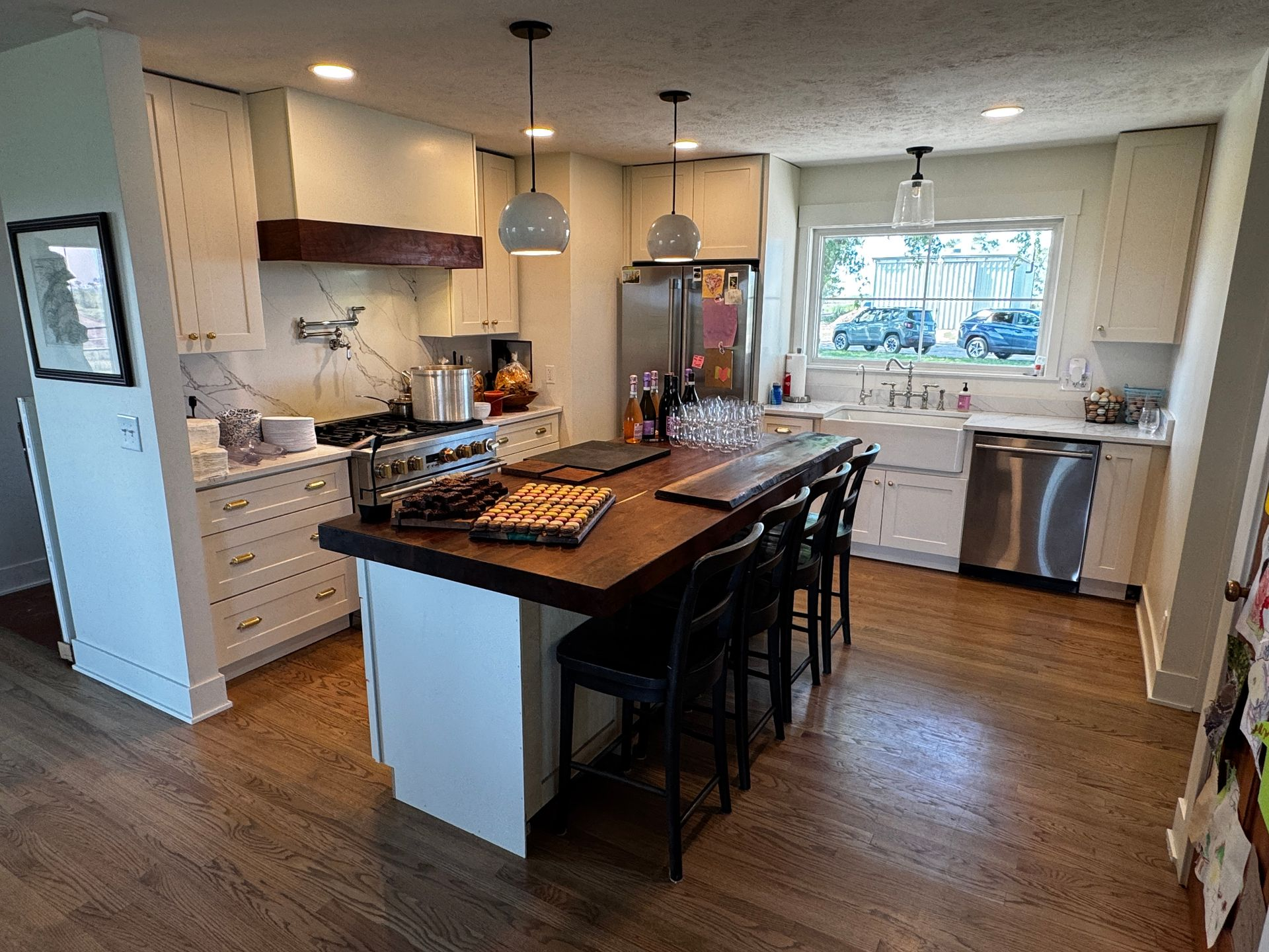 A bright, modern kitchen featuring white cabinets, a dark wood-topped island with stools, and stainless steel appliances.