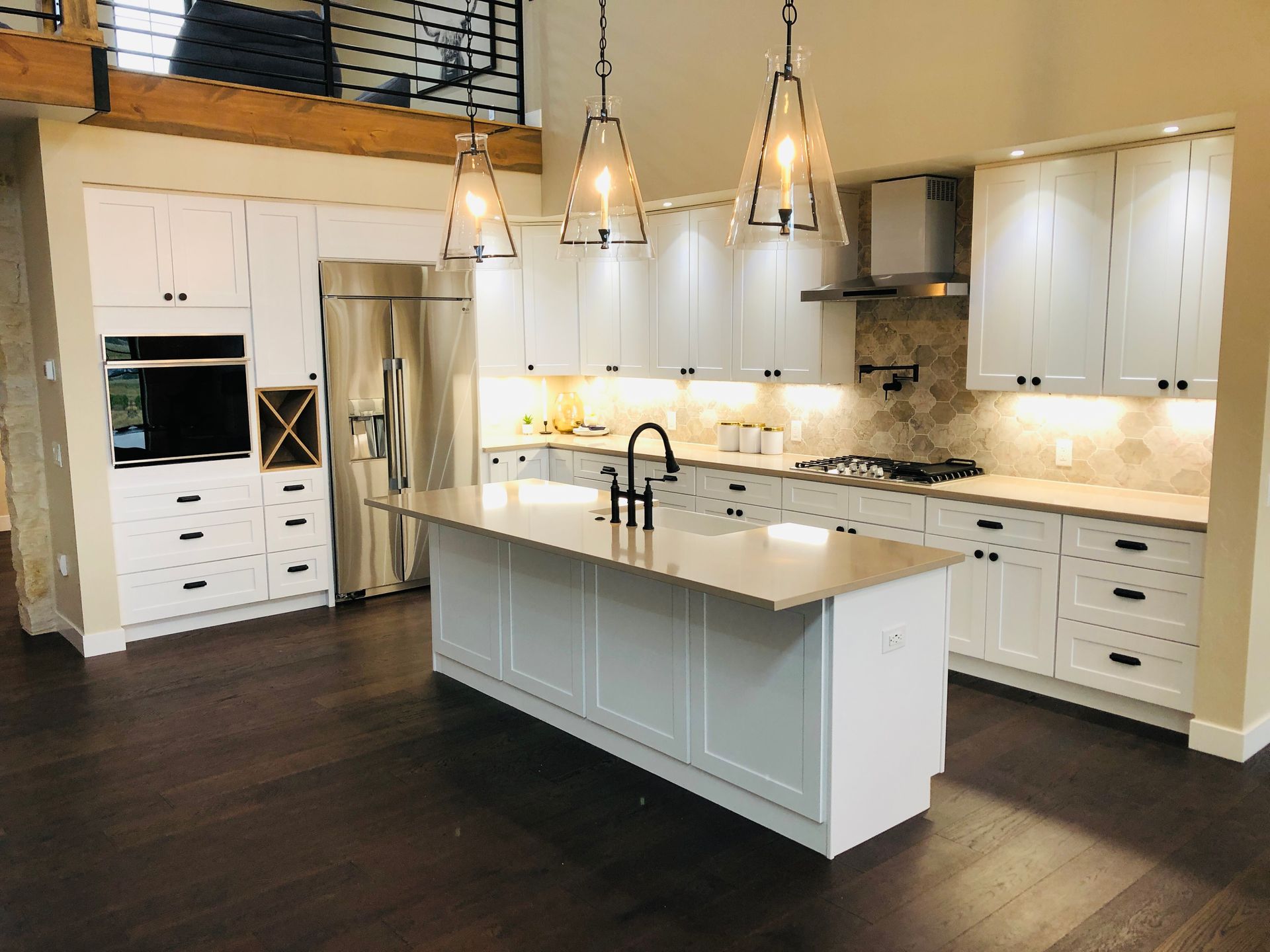 Modern white kitchen with dark wood floors, a large center island, and stainless steel appliances.