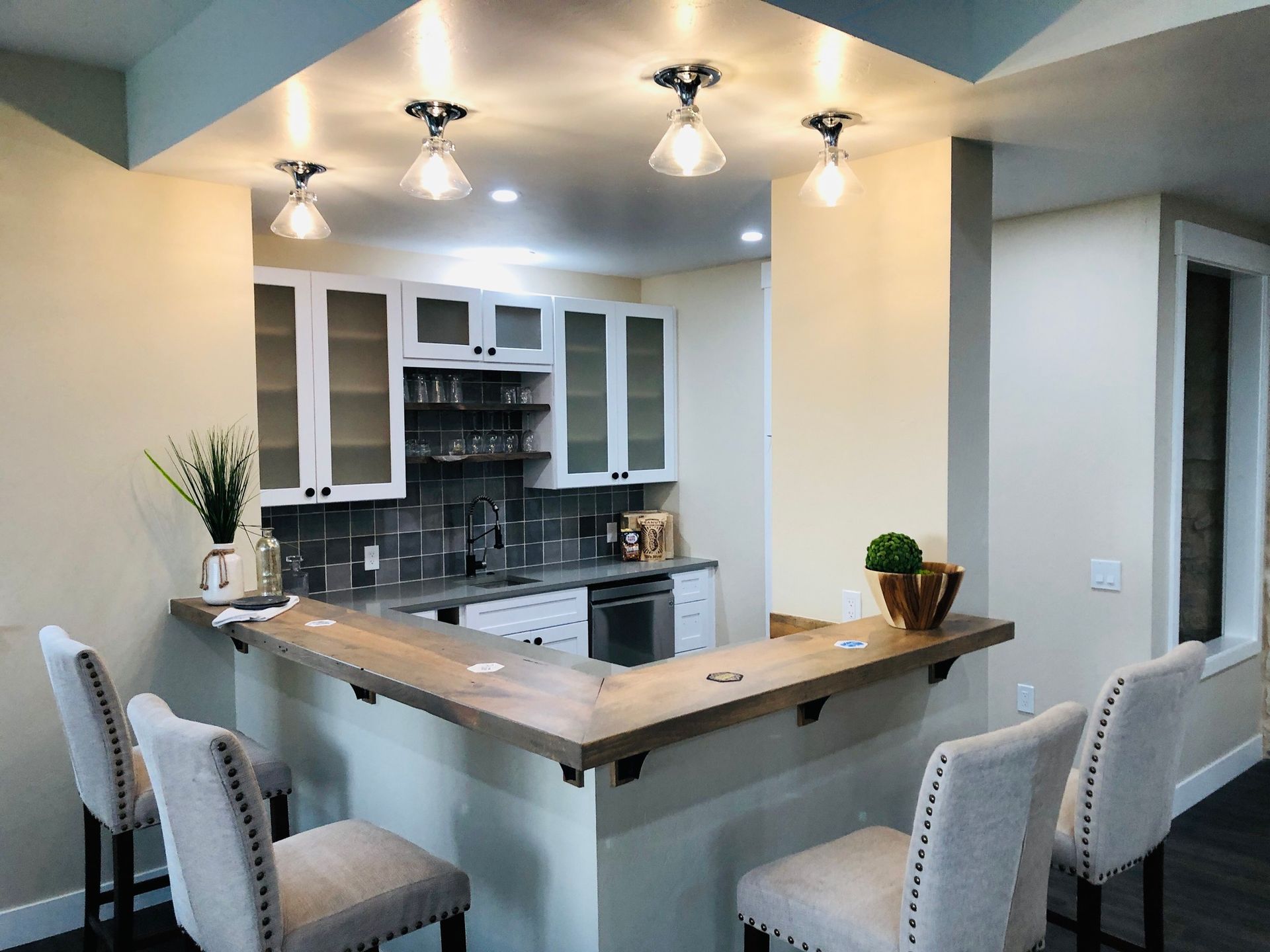 A U-shaped kitchen island with four upholstered bar stools, centered in a room with white cabinets and tile backsplash.