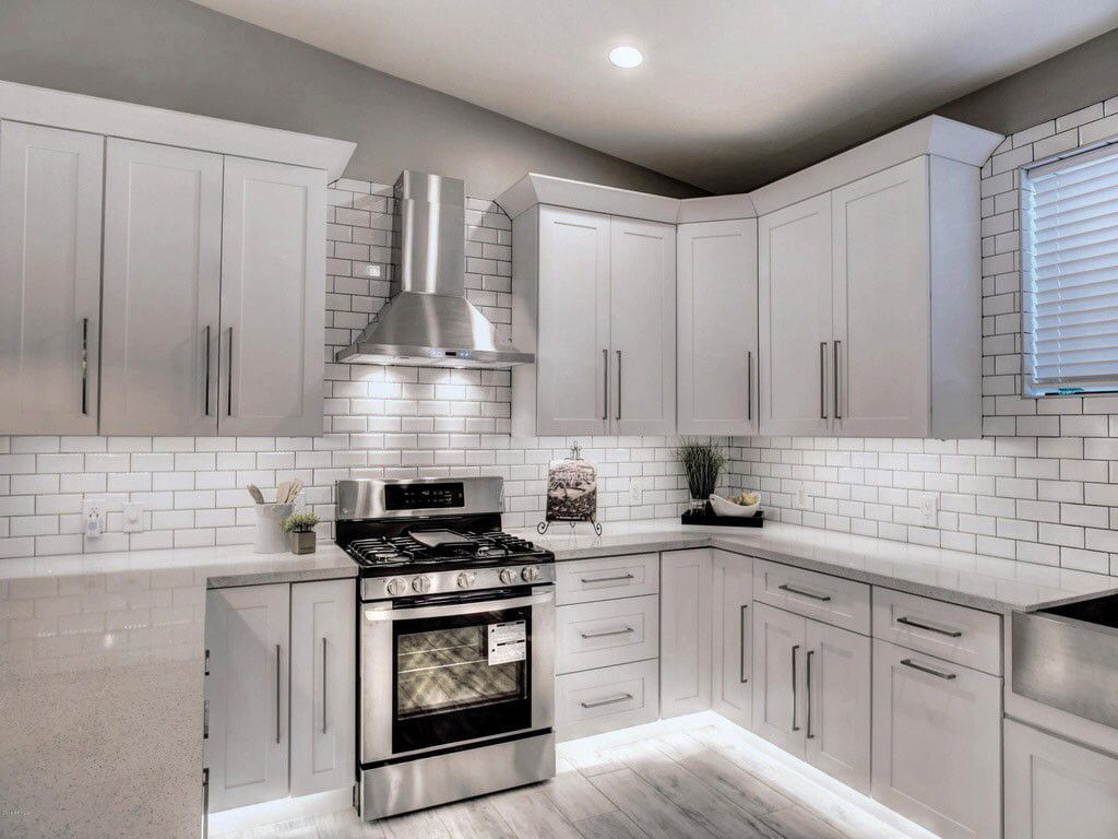 Modern kitchen with light gray cabinets, white subway tile backsplash, stainless steel appliances, and quartz countertops.
