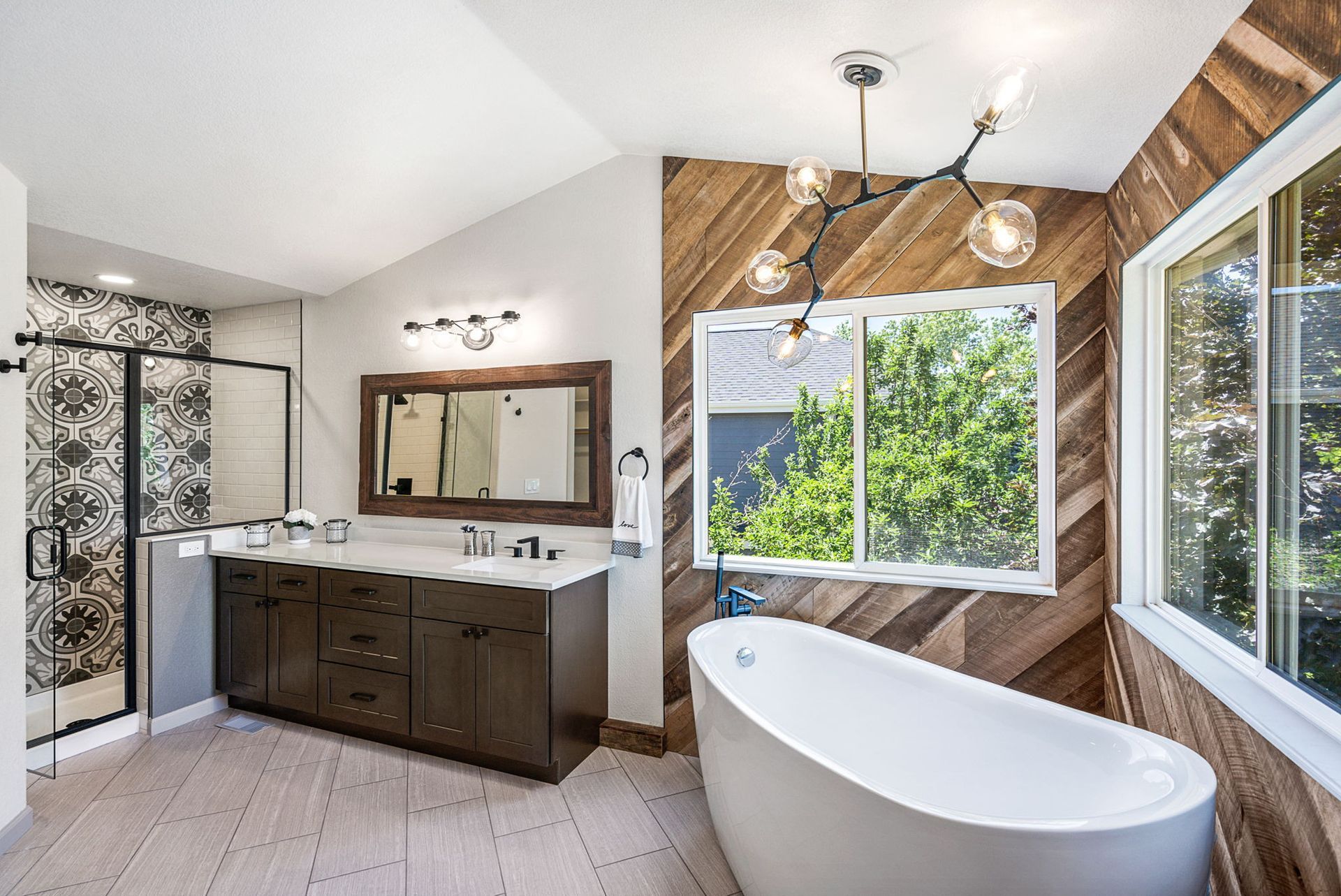 A modern bathroom featuring a white soaking tub, dark wood vanity, a glass-enclosed shower, and a diagonal wood-paneled wall.
