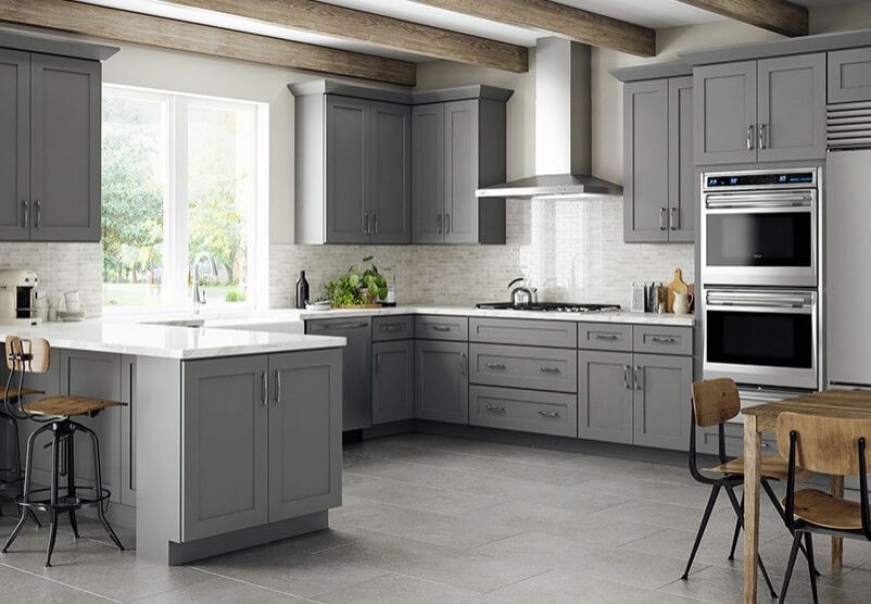 A modern kitchen featuring gray shaker-style cabinets, a stainless steel double oven, white countertops, and wood beams.
