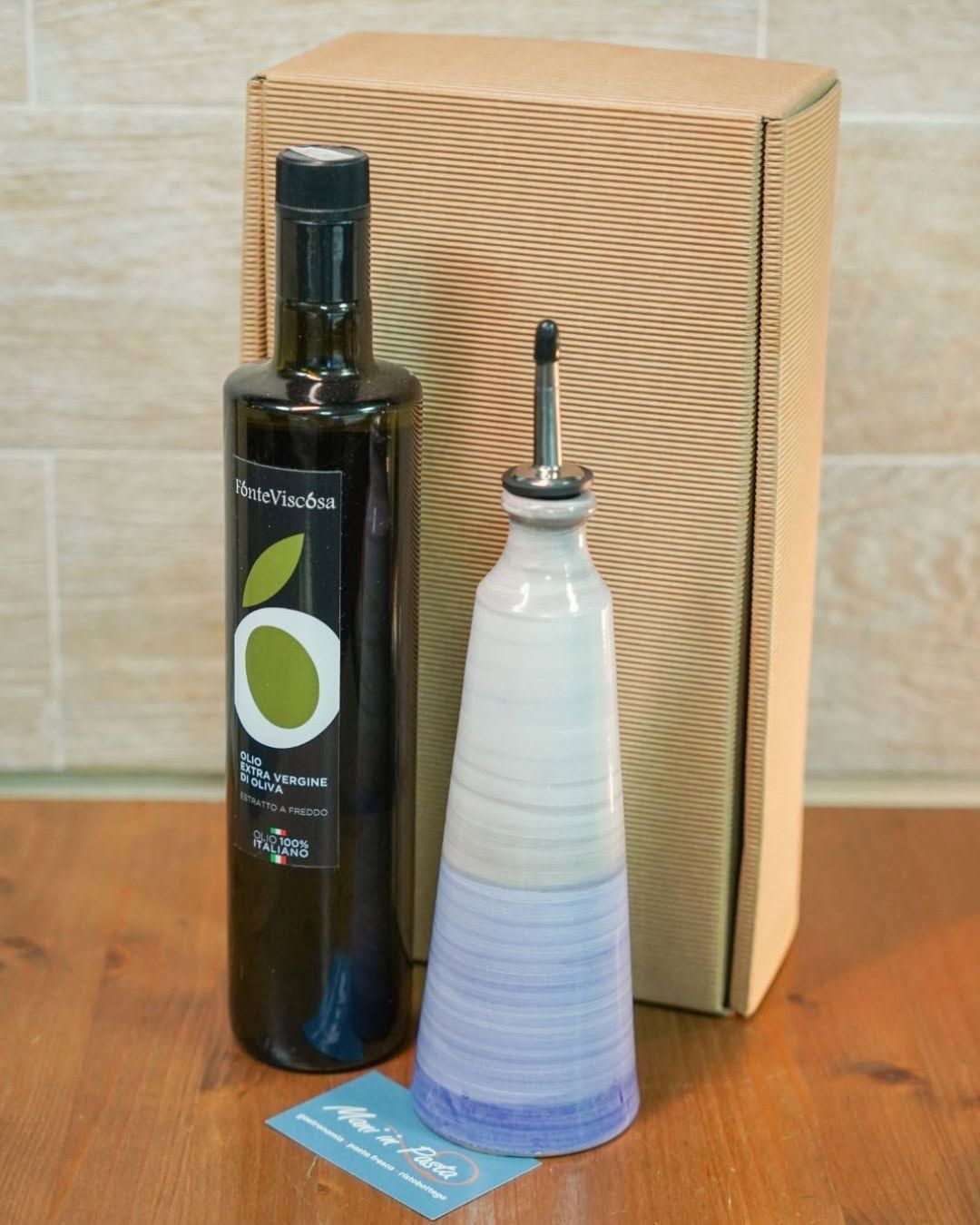 Bottiglia di olio d'oliva e dosatore di olio in ceramica su un tavolo di legno.