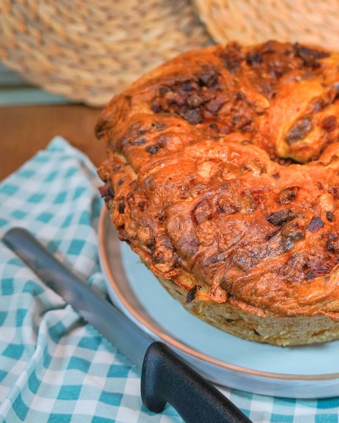 Torta salata dorata cotta al forno su un piatto accanto a una tovaglia a quadri blu e un coltello