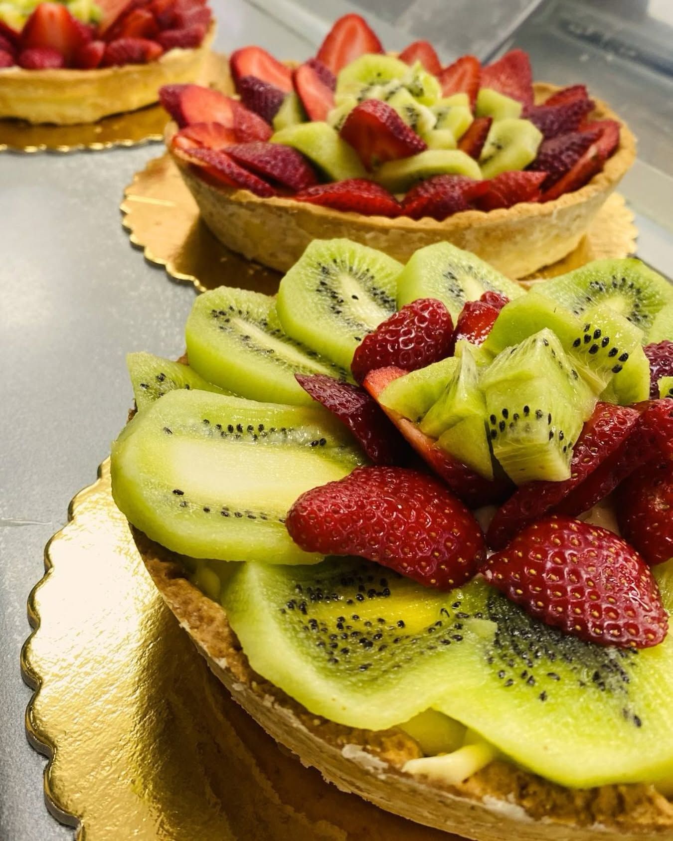 Crostatine di frutta guarnite con kiwi e fragole a fette, servite su un vassoio da pasticceria.
