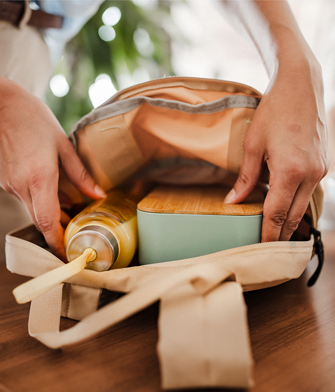 Hands packing a lunch bag with a water bottle and lunch container on a wooden table.