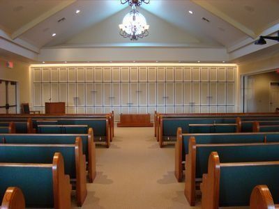 Interior of a chapel with rows of green pews facing a wooden altar and a wall of storage cabinets.
