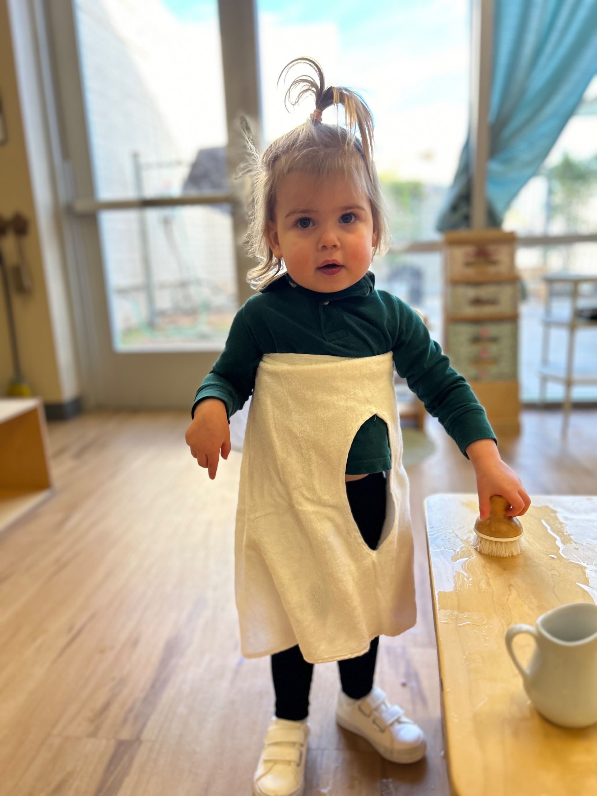 A little girl in a towel dress is cleaning a table