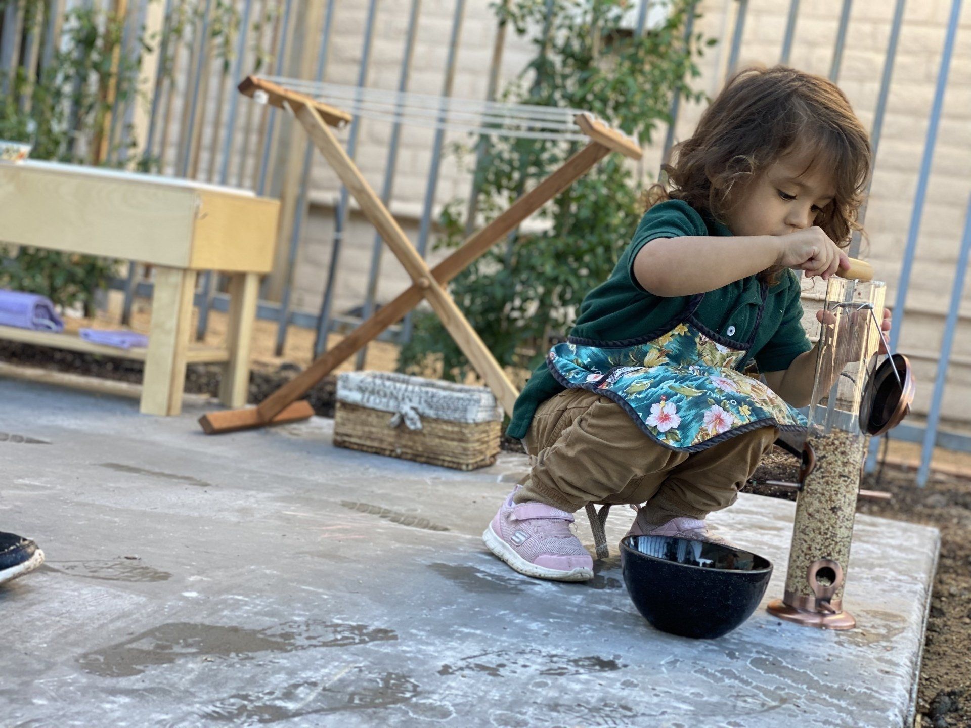 A little girl is playing with a bird feeder and a bowl of water.