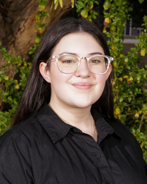 A woman wearing glasses and a floral dress is smiling for the camera.
