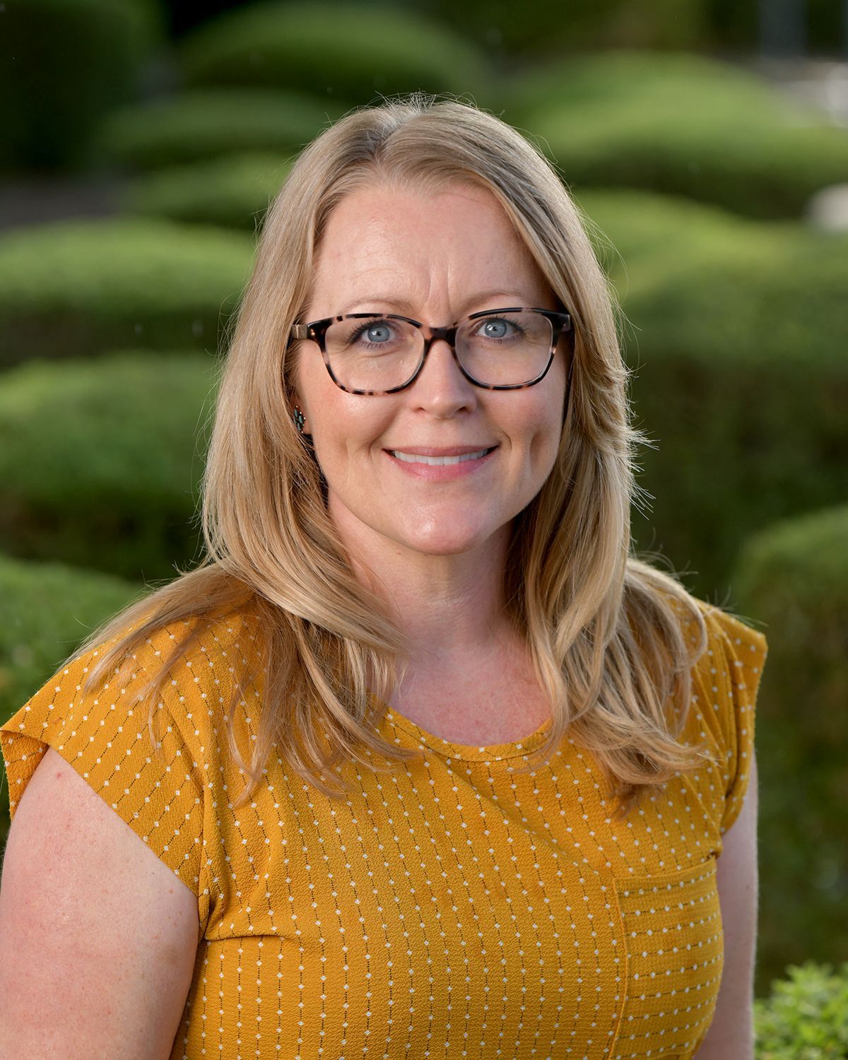 A woman wearing glasses and a yellow shirt is smiling for the camera.