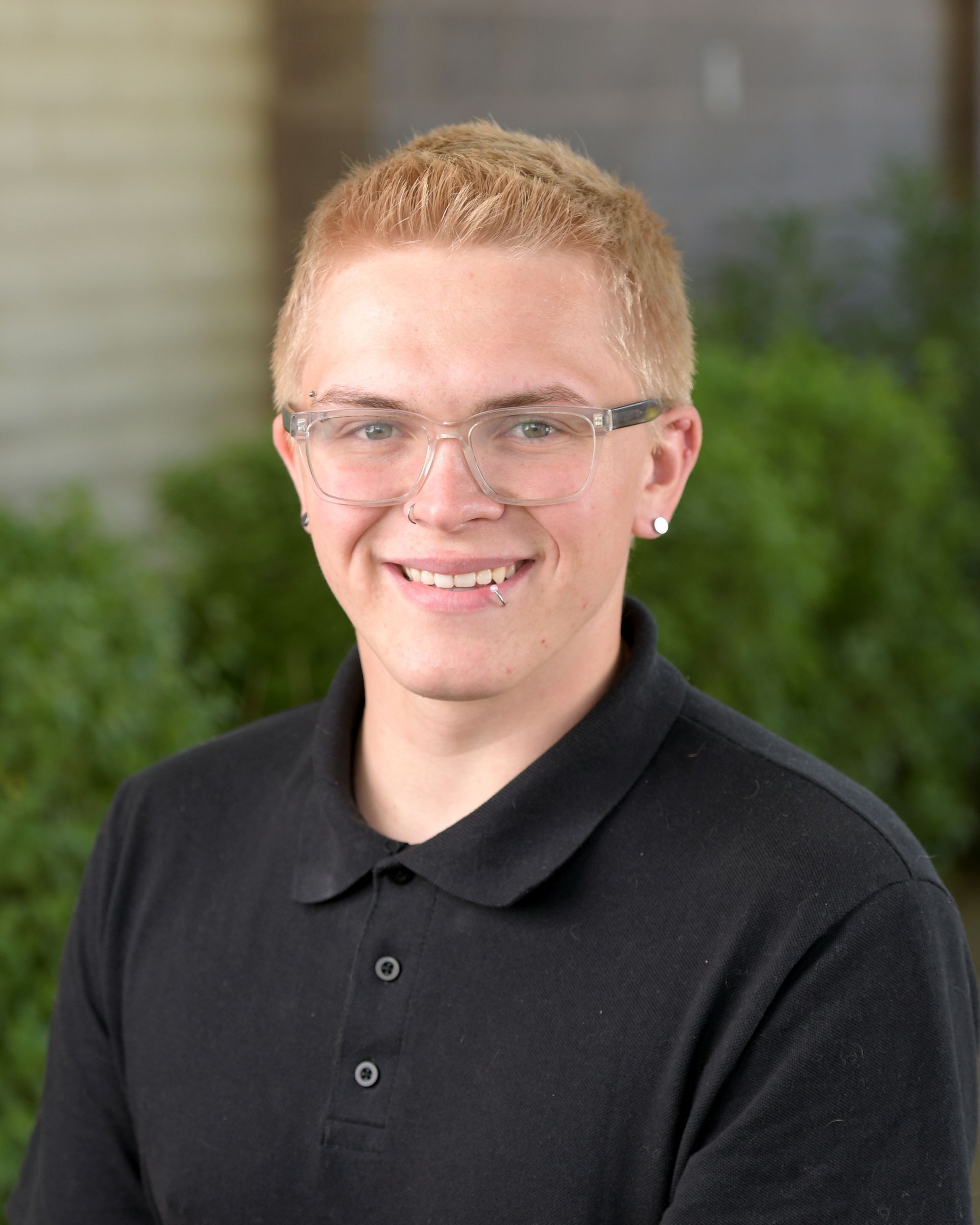A young man wearing glasses and a black polo shirt is smiling for the camera.