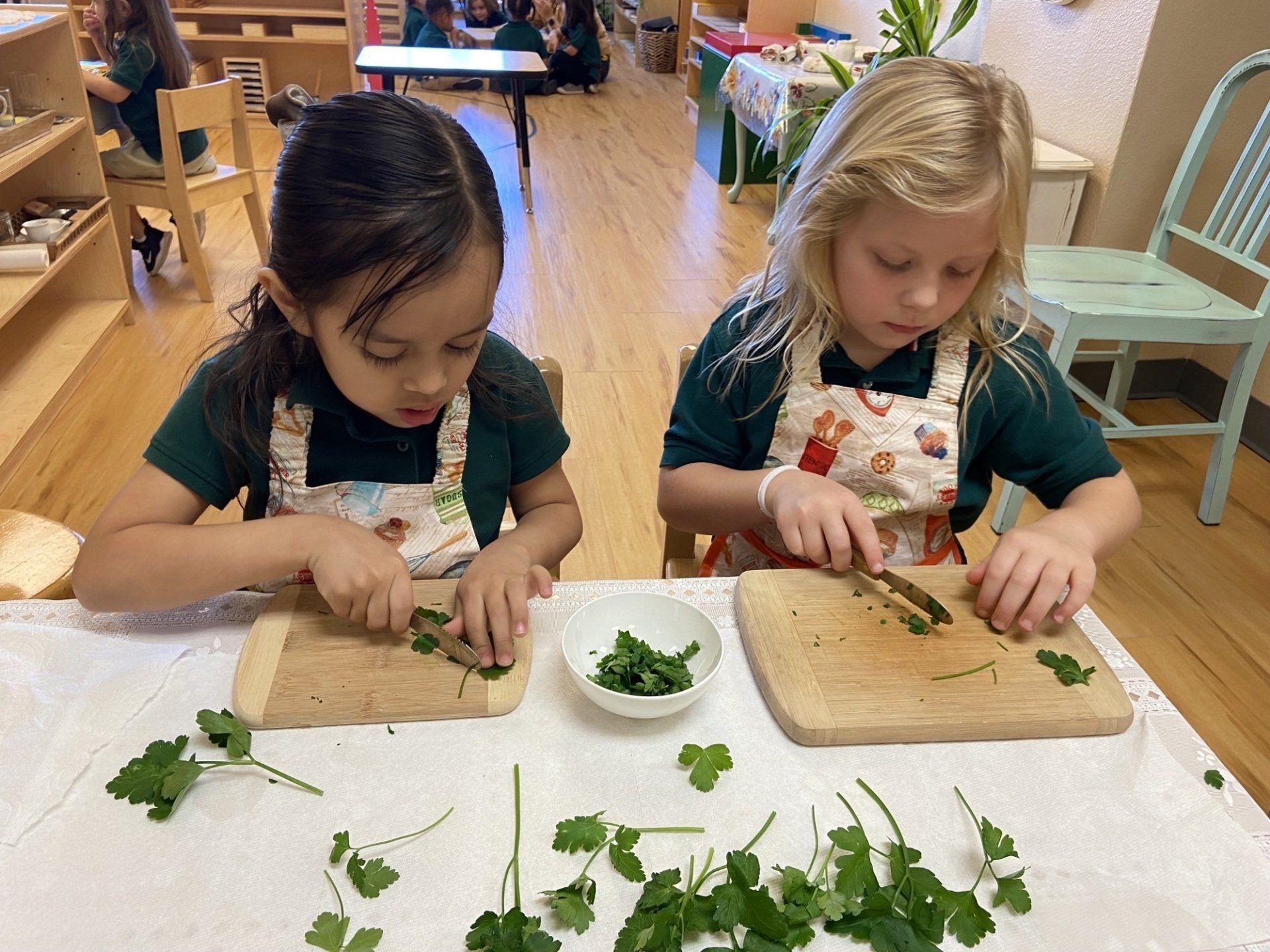 Two young girls are cutting herbs on a cutting board.
