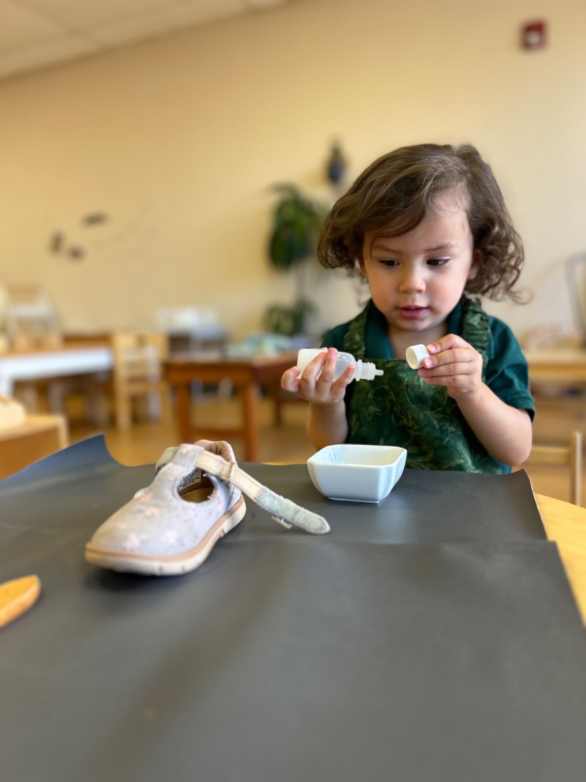 A little girl is sitting at a table playing with a shoe.