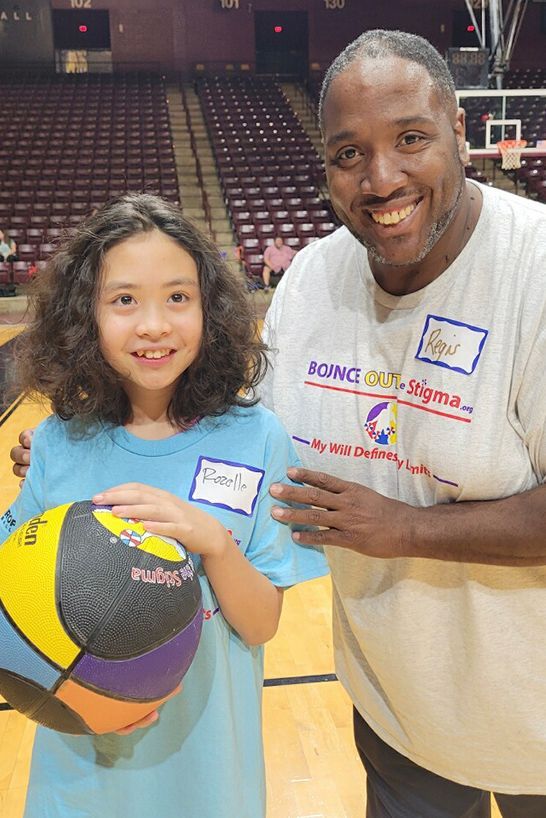 A person holding a multicolored basketball stands next to another person in a basketball arena.