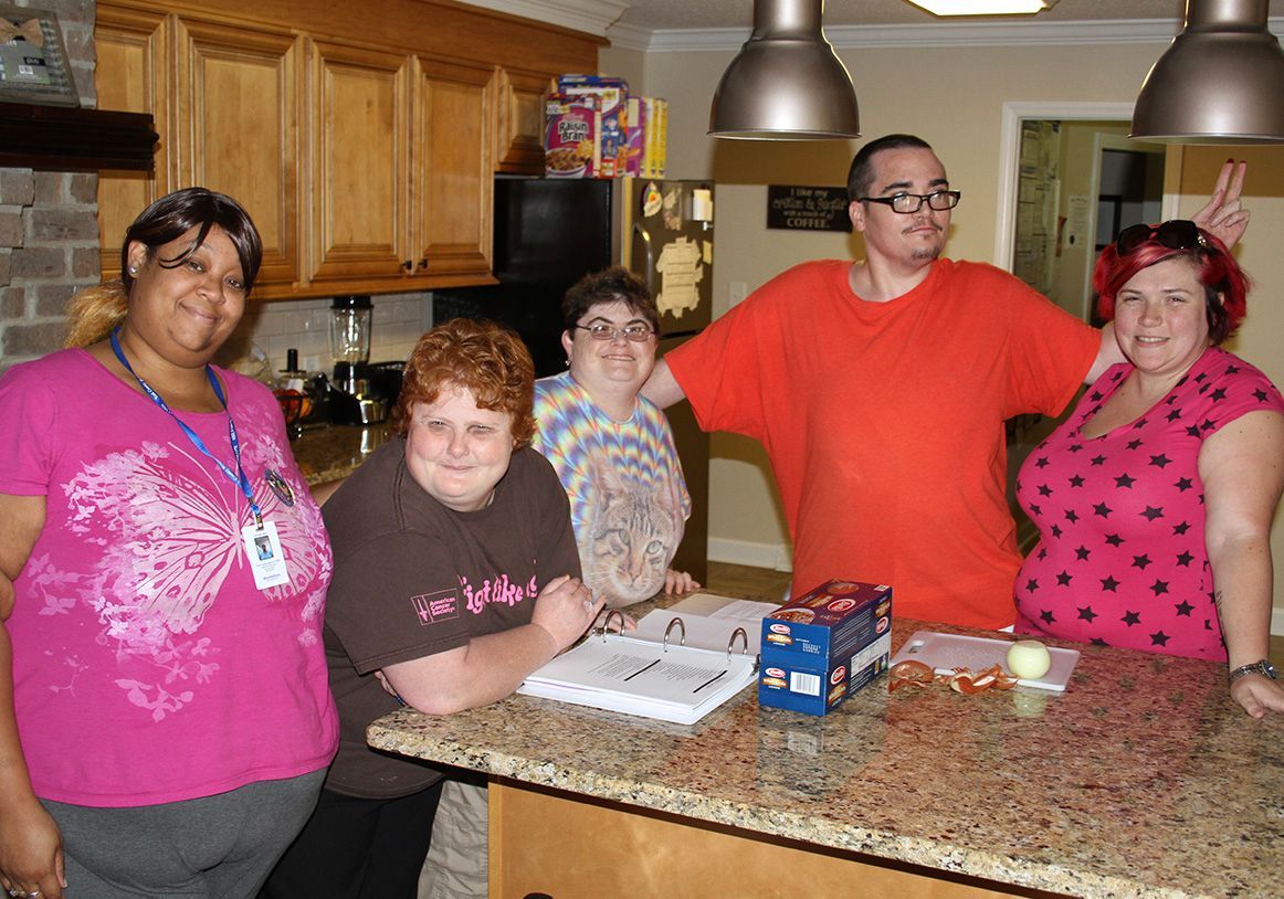 Five people stand behind a kitchen island, smiling, with one person making a hand gesture behind someone’s head. Residential Support York County SC