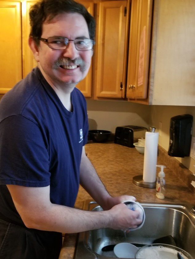 A person wearing glasses and a navy T-shirt washes dishes in a kitchen sink. Residential Support York County SC