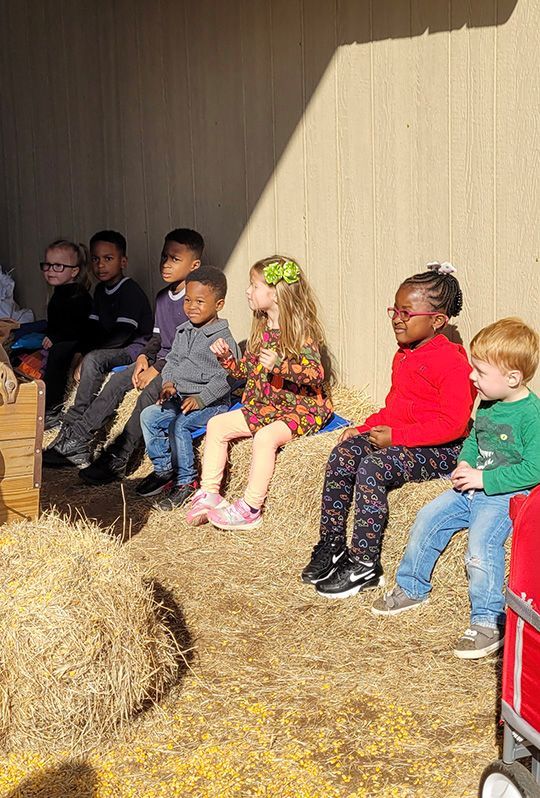 Support for children ages birth–5 with developmental delays or neurological conditions. Early intervention services in York County, SC. Early Intervention York, SC - A row of children sit on hay bales in a sunny outdoor setting.