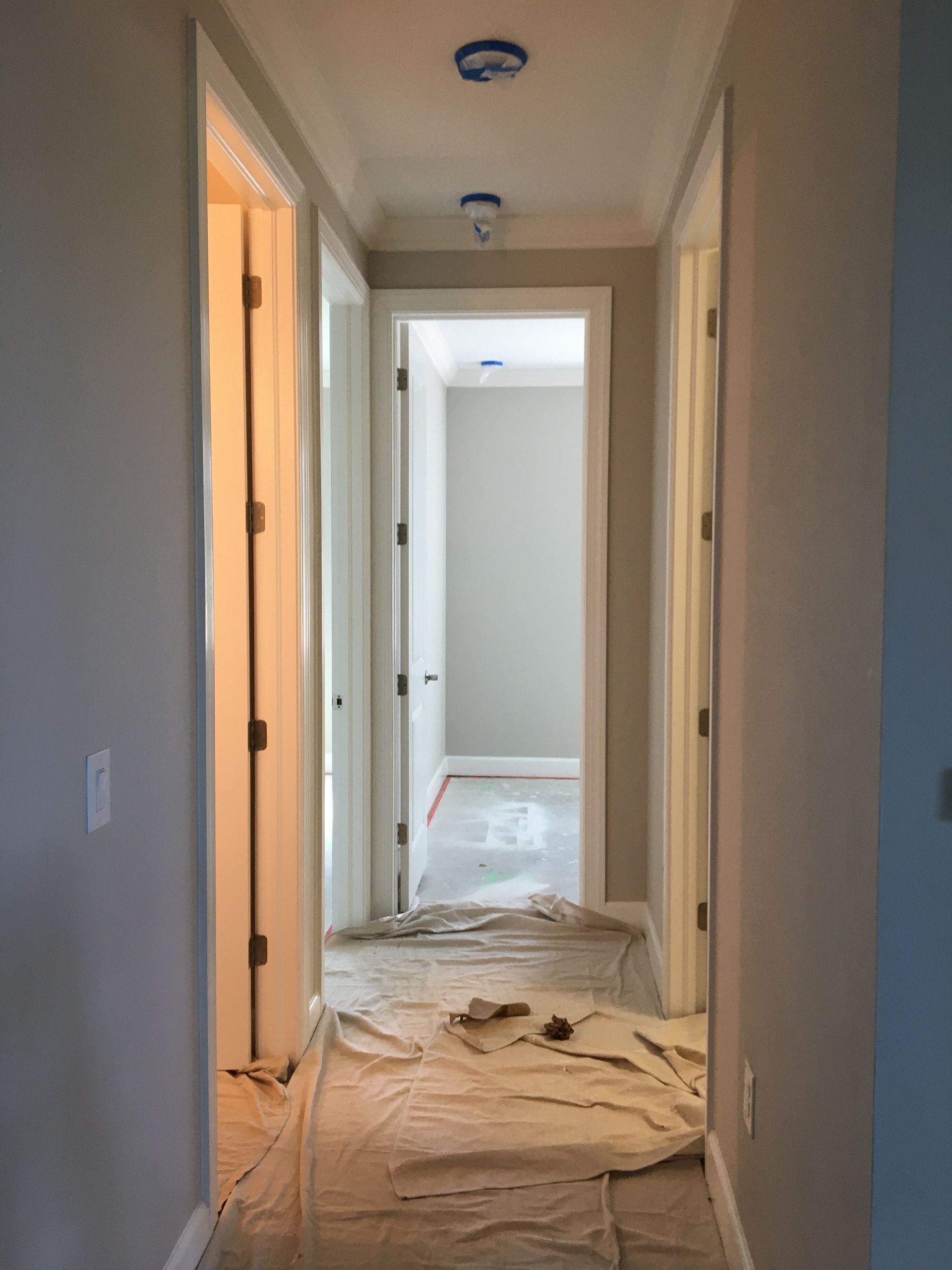 Home hallway with drop cloths and taped fixtures, ready for interior painting services near you.