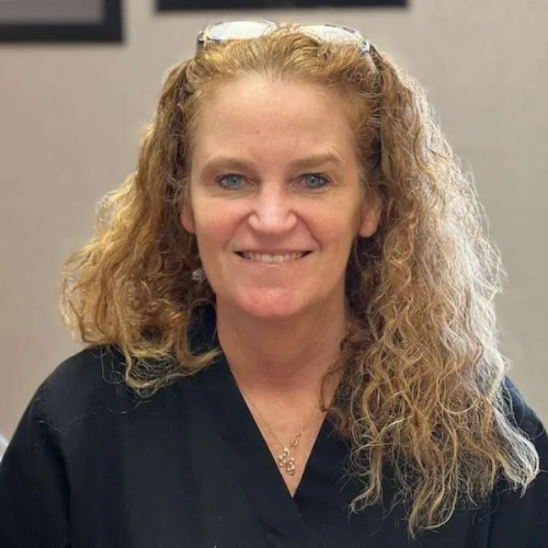 A woman wearing sunglasses and a black scrub top is smiling for the camera.