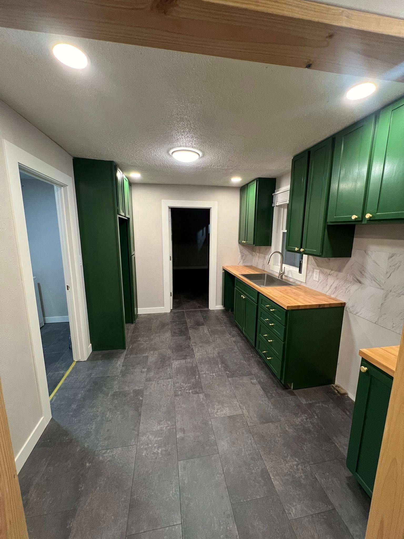 Green kitchen with dark gray flooring, wooden countertops, and white walls.