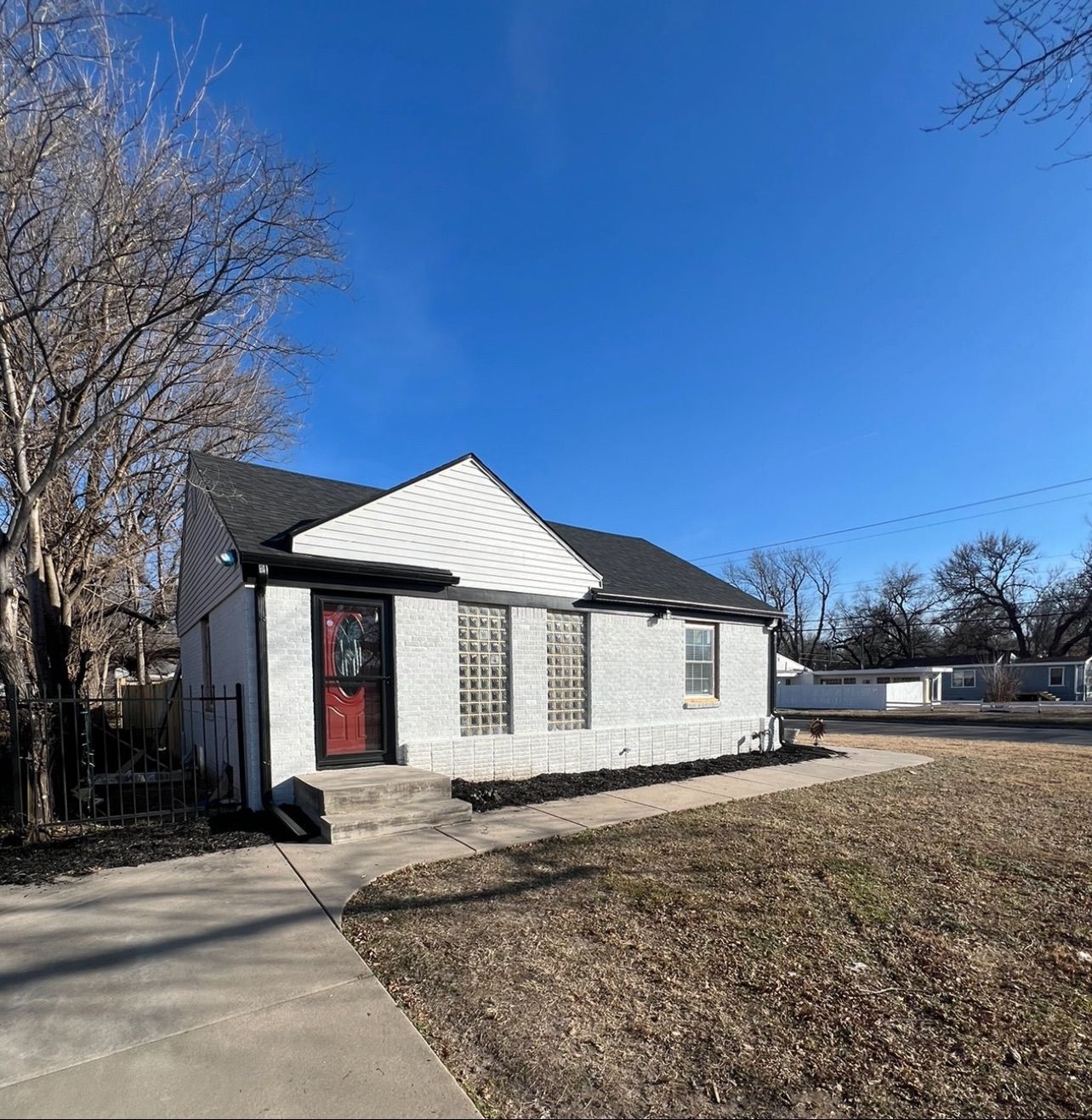 Small, white house with black trim, a red door, and a black roof against a bright blue sky.