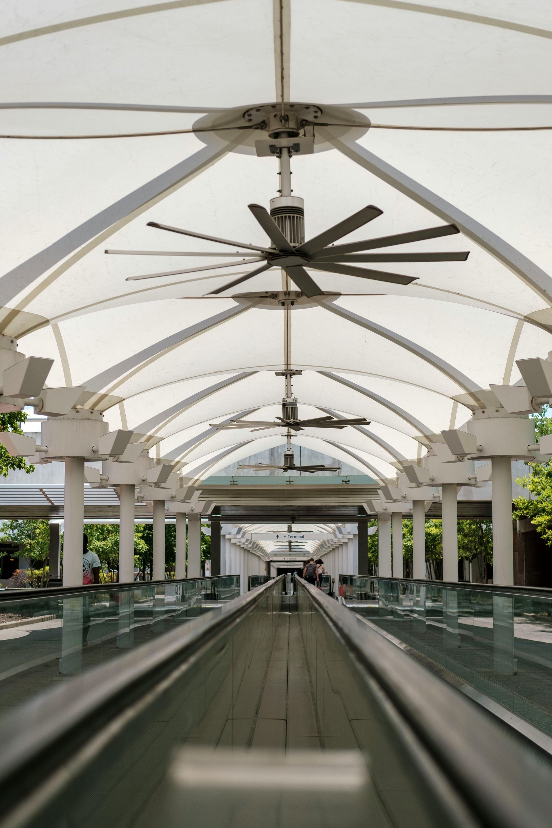 Covered walkway with moving sidewalk, ceiling fans, and white awning.