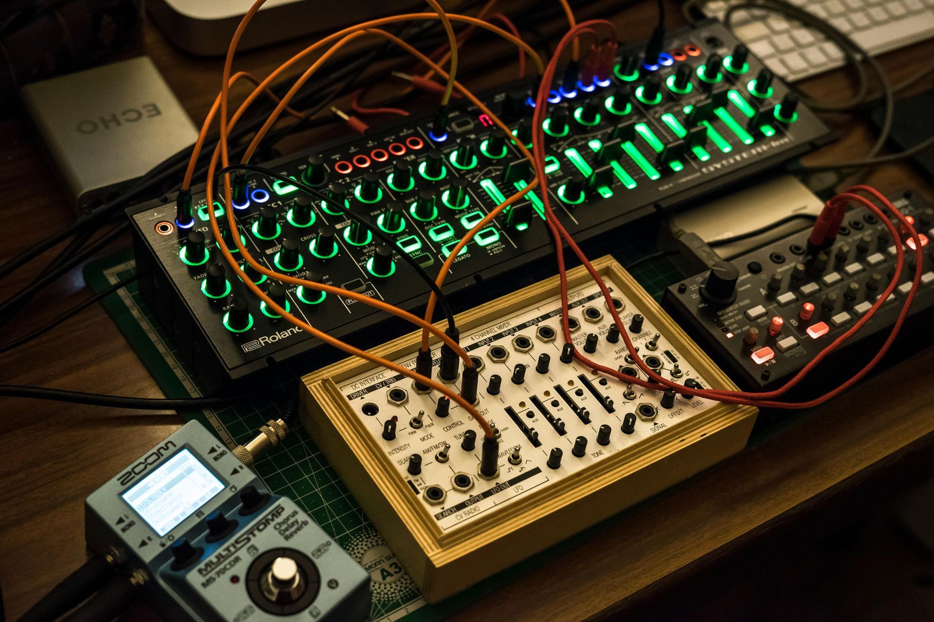 A modular synthesizer setup with multiple electronic instruments, connected by orange cables, illuminated by green lights.