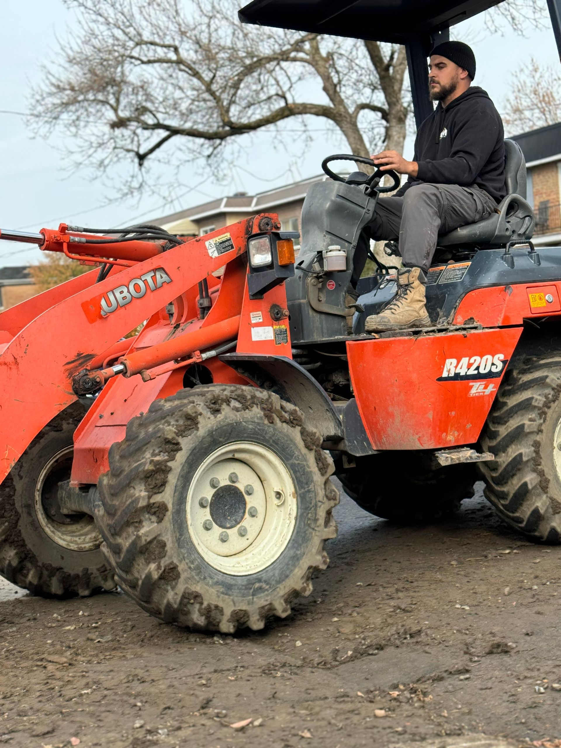 Un homme conduit un tracteur rouge sur un chemin de terre.