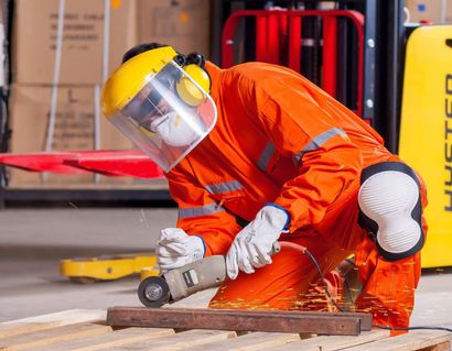 Un trabajador con equipo de seguridad naranja corta metal con una amoladora angular; saltan chispas en un taller.